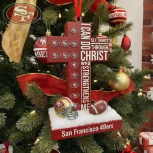 A red cross shaped ornament with team logos and small football items hangs on a Christmas tree decorated with red gold and themed ornaments.