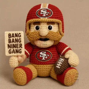Crocheted red and gold football figure holding a brown football and a stitched sign while seated.