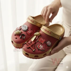 Person holding San Francisco 49ers red and gold Crocs with themed charms in bright light!