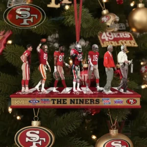 Several football figures in red and white uniforms stand on a long ornament hanging from a Christmas tree decorated with red gold and team themed baubles.