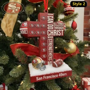A Christmas ornament featuring a 49ers themed cross with inspirational wording set on a snowy stand among holiday tree ornaments!