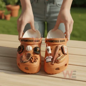Hands holding orange San Francisco Giants Crocs with baseball themed charms on outdoor wooden table!