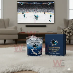 A San Jose Sharks branded glass with ice beside a matching anniversary box positioned on a fluffy rug in a living room with a televised hockey game visible behind them!