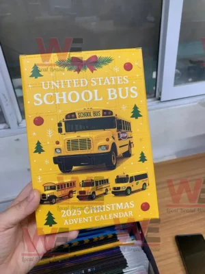 A close up of a person holding the yellow United States School Bus 2025 Advent Calendar box decorated with buses and festive icons.