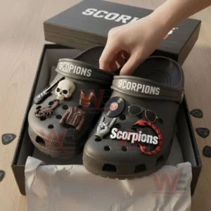 Hand picking up gray Scorpions clogs with themed charms from an open branded box.