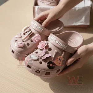 Hands holding pink Selena Gomez clogs with stylish charms and soft decorative details.