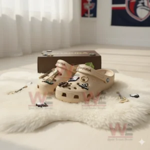 Beige Shakira Crocs with music themed charms placed on white rug in bright room near brown box!