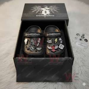 Black clogs with Shinedown decorations placed in a branded black gift box on a white fluffy rug.