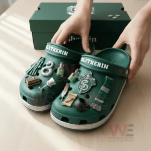 Green clogs adorned with themed charms placed on a wooden table near a green box.