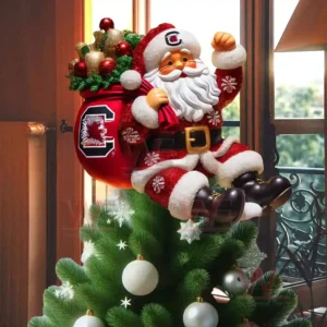 Santa Claus wearing a red South Carolina Gamecocks outfit sitting on top of a Christmas tree holding a red gift sack decorated with the Gamecocks logo!