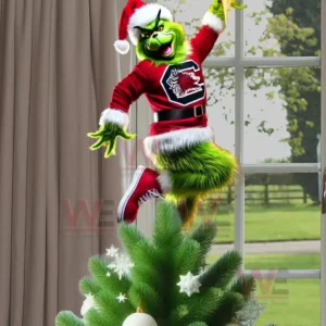 The Grinch wearing a red South Carolina Gamecocks sweater and Santa hat posing energetically on top of a Christmas tree inside a bright room!