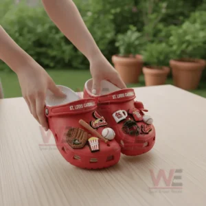 Hands holding red St Louis Cardinals Crocs with baseball themed charms on wooden table outdoors!
