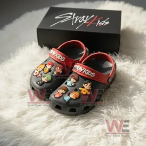 Black Crocs style shoes with red Stray Kids straps and multiple colorful cartoon charms on the top displayed on white fur!