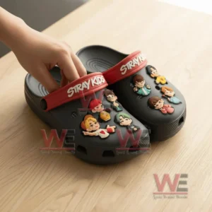Close up of Stray Kids Crocs with red straps and multiple character charms as a hand adjusts one shoe!