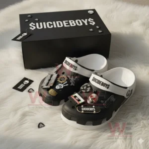 Black and white clogs with Suicideboys decorations placed beside a black logo box on a soft rug.