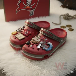 Red Buccaneers Crocs with themed charms like ship and trophy placed beside team box on white surface!