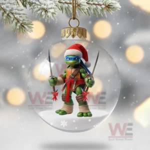 A clear ornament with a Santa hat ninja turtle holding swords standing over a snowy base with winter lights behind it!