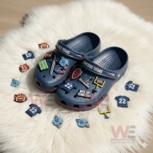 Navy blue Tennessee Titans Crocs with scattered football charms including helmets and jerseys on a white rug.