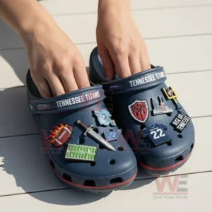Hands holding navy blue Tennessee Titans Crocs with football charms including logo and jersey number 22.