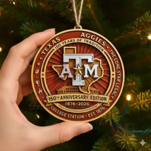 Close up of a hand holding a Texas A&M Aggies 150th anniversary ornament with detailed design and festive tree lights in the background.
