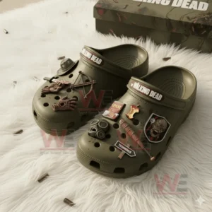 Olive green The Walking Dead Crocs with survival themed charms including weapons and zombie designs on a white rug.