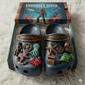 Blue clogs with undersea charms placed inside an open box resting on a white fluffy rug.