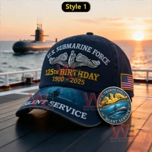 A navy blue U.S. Submarine Force 125th Birthday cap with a submarine design on the brim displayed near a ship at sunset.