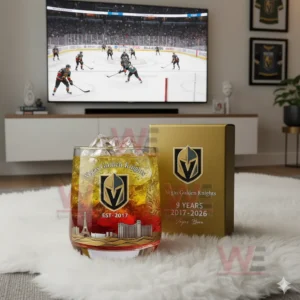 A whisky glass with team branding and city skyline sits on a white rug with a hockey game visible on a television in the background.