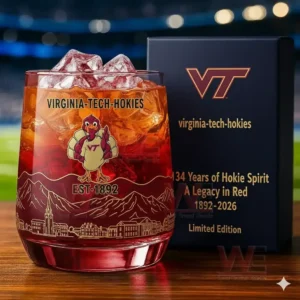 Virginia Tech Hokies 134th Anniversary Whiskey Glass 3 Alt text: A close-up of a whiskey glass with the Virginia Tech Hokies logo and a commemorative anniversary box, set against a football field backdrop.