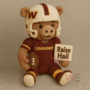 Crocheted maroon and white football themed animal figure holding a brown football and a stitched sign while seated.