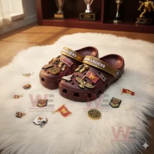 Maroon Washington Commanders Crocs surrounded by scattered charms like logos and trophies on a soft rug.