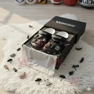 Black Wednesday clogs with multiple charms arranged in an open box on a fluffy white surface.