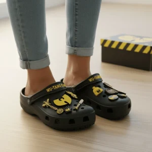 Person wearing Wu Tang Clan Crocs with gold themed charms indoors.