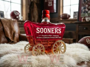 130 Years Of Oklahoma Football 1895-2025 Whiskey Bottle 6 Commemorative red wagon bottle with gold wheels and red stopper displayed among football collectibles!