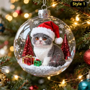 A longhaired cat in a Santa hat sitting inside a clear ornament with red trees and presents on a Christmas tree!