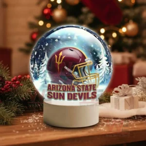 A snow globe with a maroon team helmet inside sits on a wooden table among holiday decorations and soft lights!