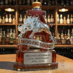 Arkansas Razorbacks 132nd Anniversary Woo Pig Sooie Whiskey Bottle 5 Razorbacks commemorative whiskey bottle with crowned letter A and metallic razorback displayed on a bar counter with bottle shelves in the background.