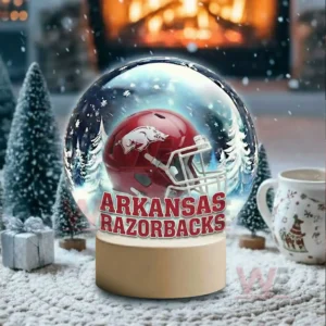A snow globe with a red team helmet sits in a snowy room with a glowing fireplace and holiday decor!