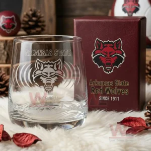 Arkansas State Red Wolves Whiskey Glass 6 A transparent glass with etched graphics of the Arkansas State Red Wolves logo positioned in a cozy rustic setting near a branded box!