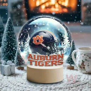 A snow globe with a dark blue team helmet sits in a snowy room with a glowing fireplace and holiday decor!