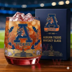 A close view of an Auburn Tigers themed whiskey glass filled with an amber drink accompanied by a navy box printed with the team logo and campus illustration!