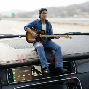 A rock musician figure with a guitar sitting on a car dashboard above a digital music display during a road trip!