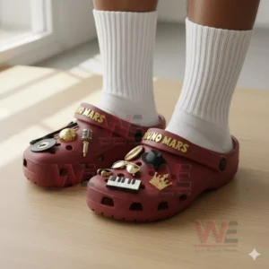A close up view of red crocs covered in gold and black music themed charms inspired by Bruno Mars worn with white socks!