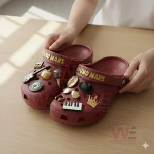 A pair of red crocs decorated with various music related charms being held on a wooden table!
