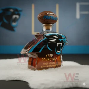 Carolina Panthers Keep Pounding 30th Anniversary 1995-2025 Whiskey Bottle 5 A Panthers emblem bottle shown at an angle resting on a fluffy white surface with sports decor behind it!