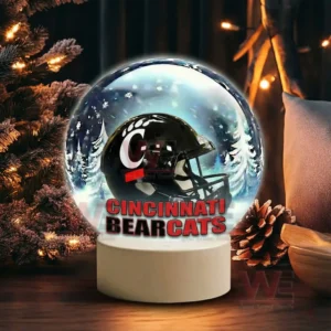 A snow globe with a black team helmet sits near pinecones greenery and warm festive lights!