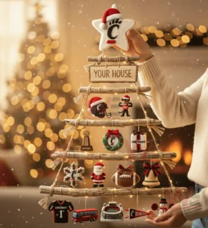 A person holding a rustic wooden branch Christmas wall tree decorated with Cincinnati Bearcats ornaments in a festive living room!