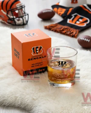 A Cincinnati Bengals anniversary glass next to an orange box placed on a fluffy surface with fan items nearby!
