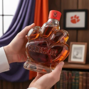 Clemson Tigers Logo Whiskey Bottle 6 Hands holding a paw shaped bottle with amber liquid in a cozy interior with framed decor!