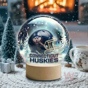 A snow globe with a dark blue team helmet sits in a snowy room with a glowing fireplace and holiday decor!